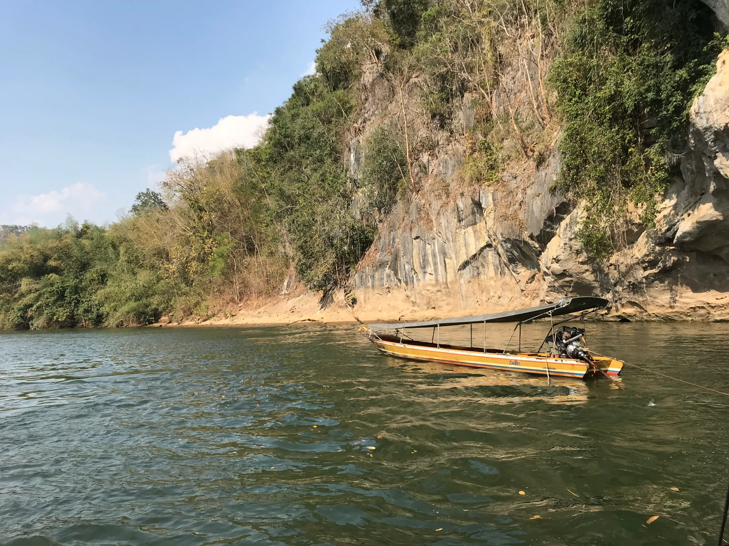 A longtail boat moored beneath a limestone cliff on the green River Kwai.