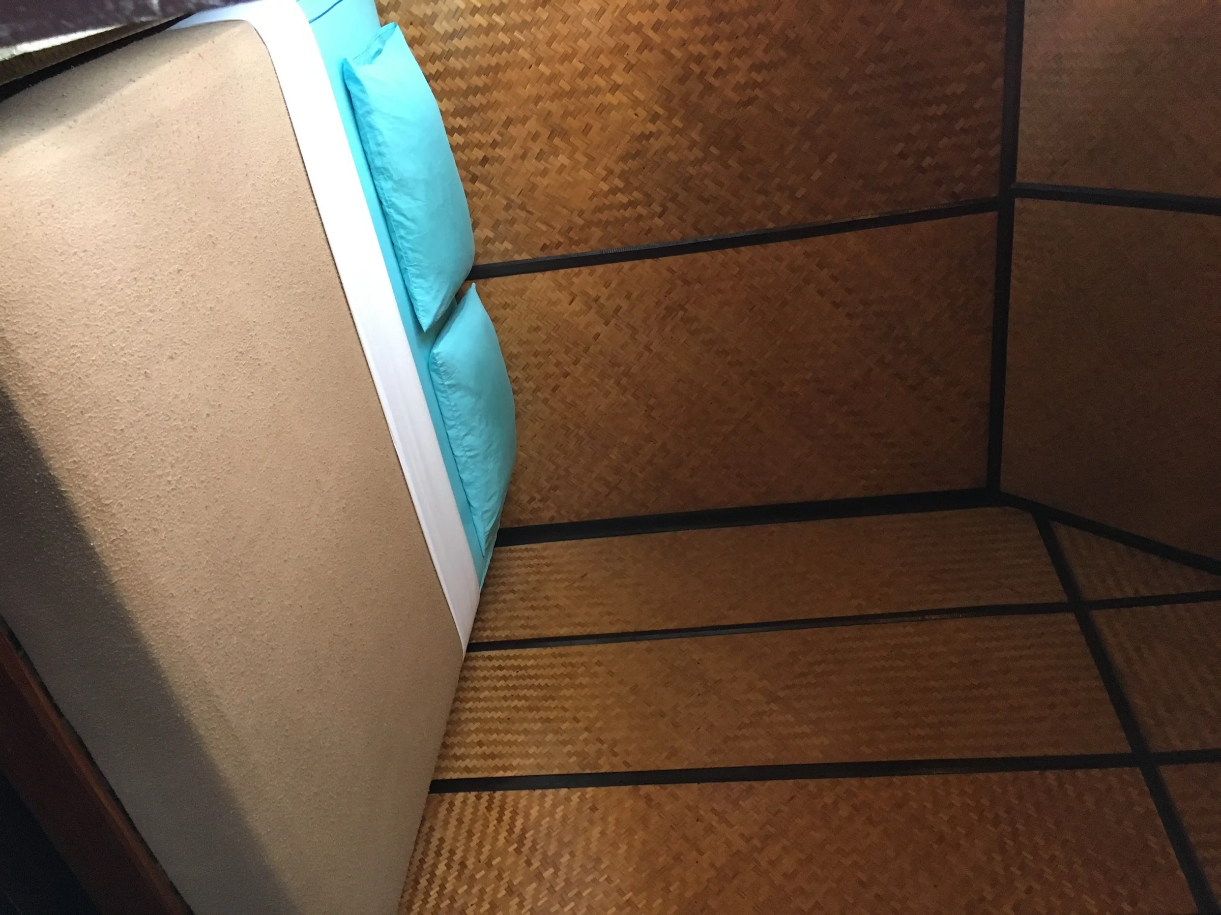A simple bungalow bedroom with woven bamboo walls and turquoise pillows at Krit Raft House.