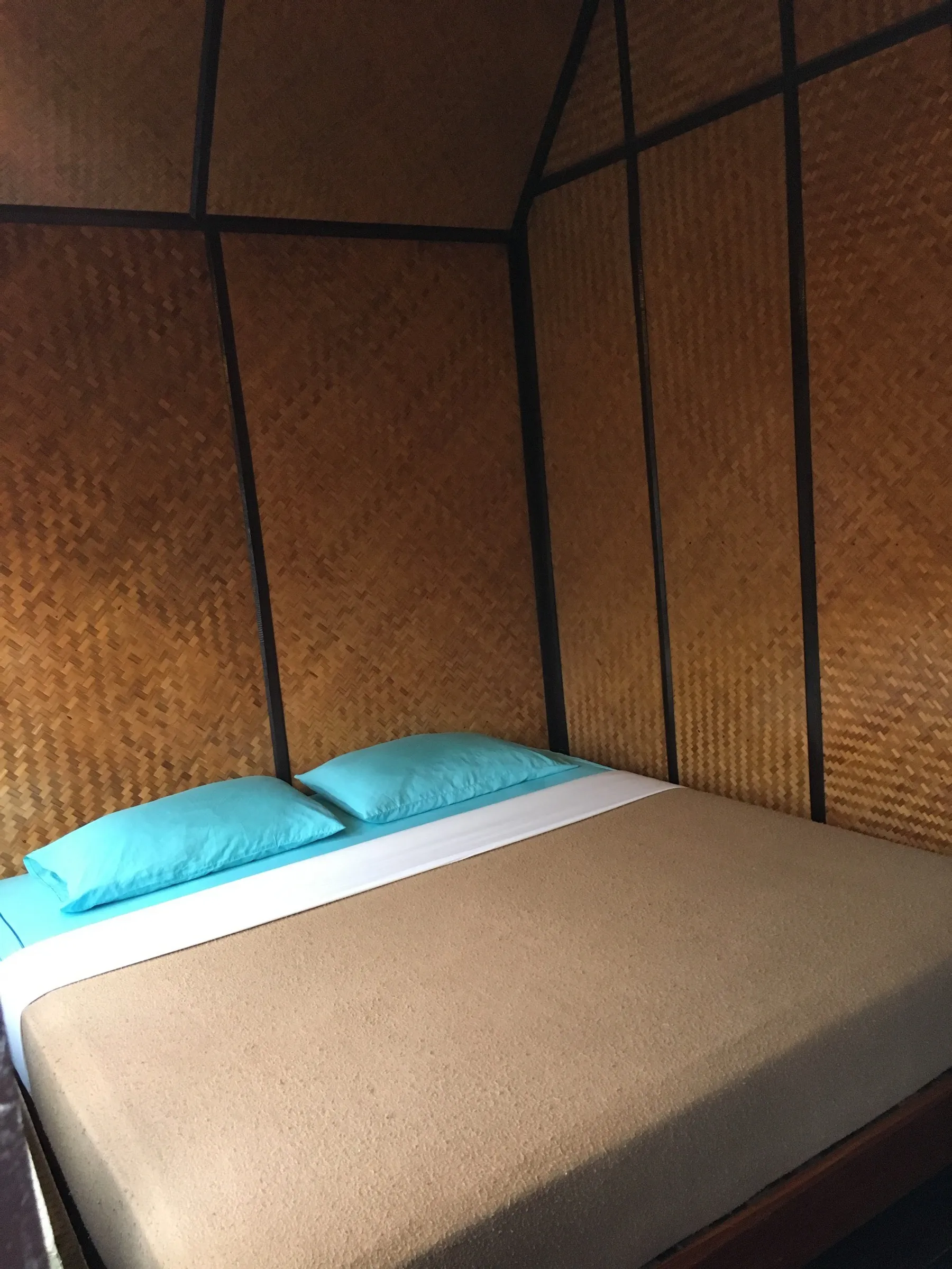 A simple bungalow bedroom with woven bamboo walls and turquoise pillows at Krit Raft House.