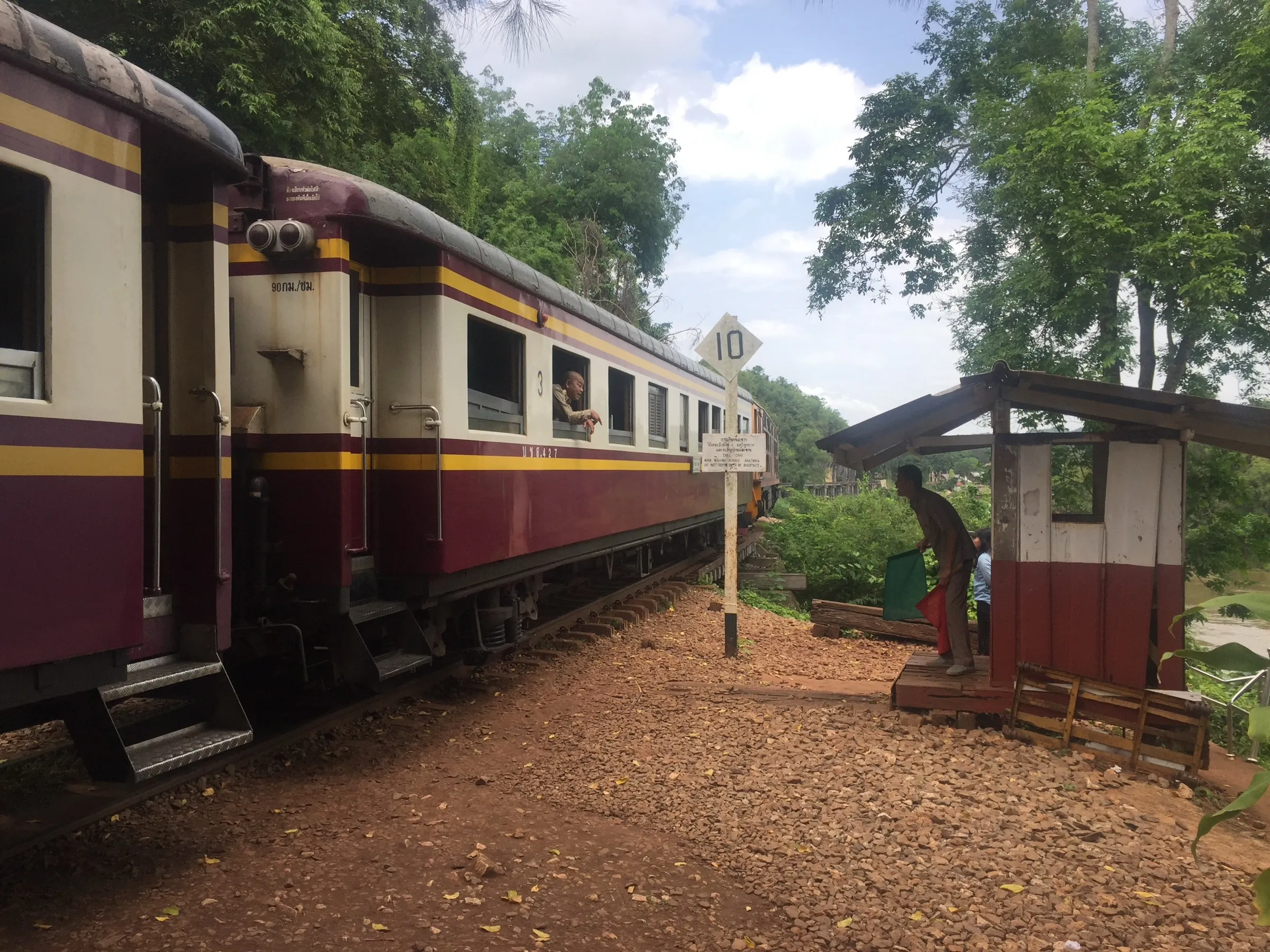 A maroon and cream third-class Thai train stopped at Nam Tok railway station.