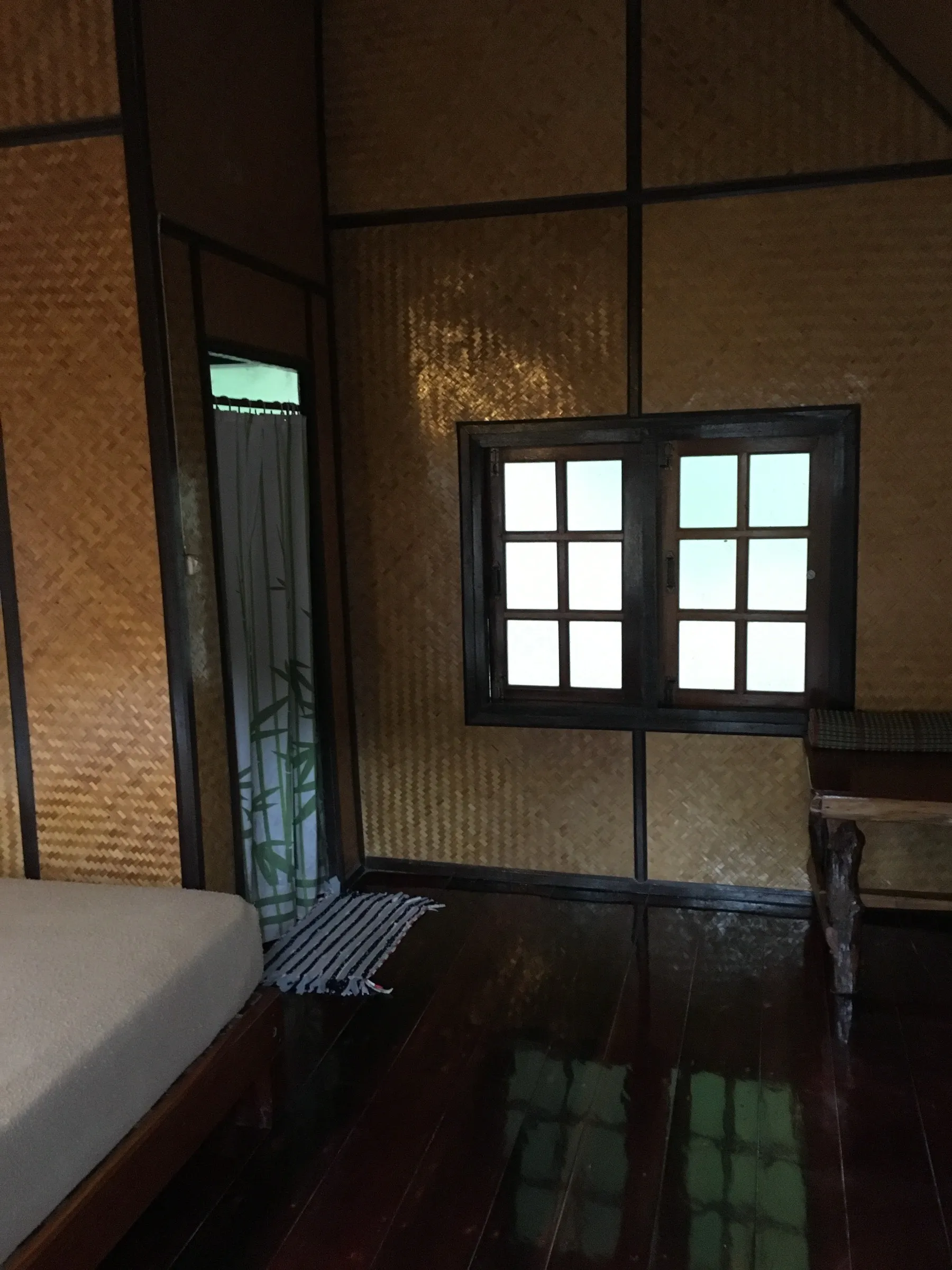 Inside a simple bungalow at Krit Raft House, woven bamboo walls and a window over the river.