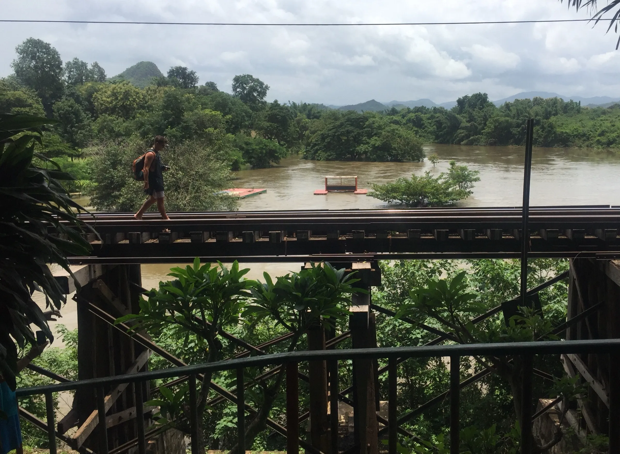 A traveller walking across a railway bridge over the River Kwai, hills beyond.